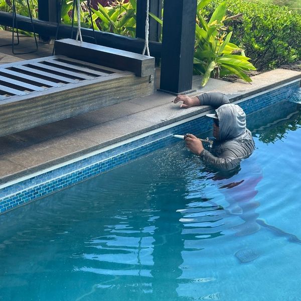 Da Pool Guy technician in a hooded shirt meticulously cleaning the waterline and tile of a residential pool. Da Pool Guy technician in a hooded shirt meticulously cleaning the waterline and tile of a residential pool.