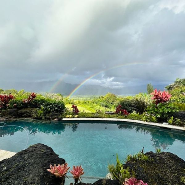 Stunning infinity pool in Kauai with a double rainbow arching over the lush green valley and dark mountains. Stunning infinity pool in Kauai with a double rainbow arching over the lush green valley and dark mountains.