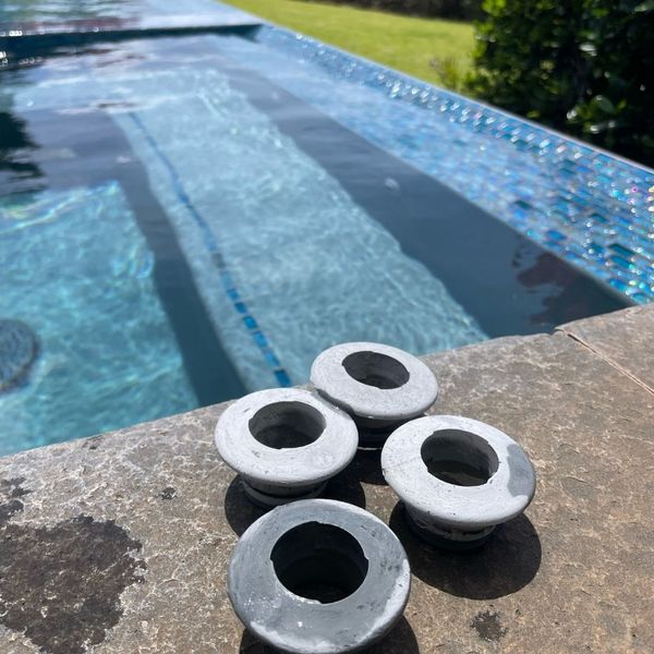 Four pool skimmer plugs resting on the wet stone coping next to a sparkling infinity pool with blue mosaic tile. Four pool skimmer plugs resting on the wet stone coping next to a sparkling infinity pool with blue mosaic tile.