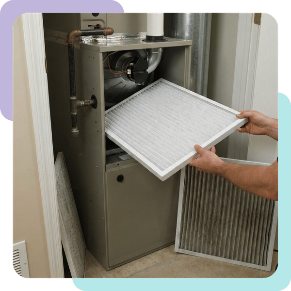 An HVAC technician replacing a dirty air filter with a clean one in a home furnace unit.