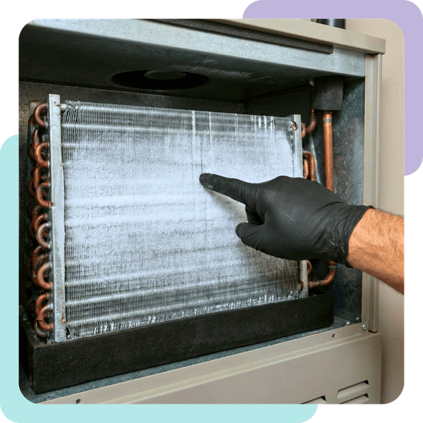 A technician's hand pointing to a frosted evaporator coil inside an indoor air handler unit.