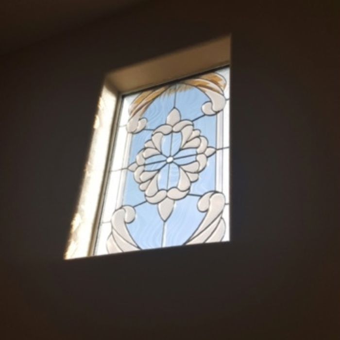 A square decorative glass window insert with a floral and scrollwork design set into a white interior wall.