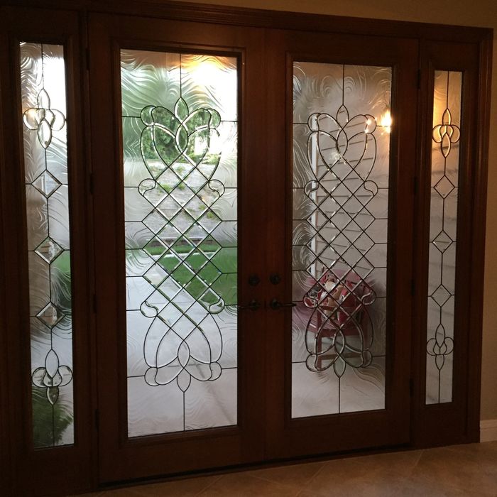 A set of dark wood double doors and sidelights with matching interlaced decorative glass patterns looking out onto a bright green lawn.