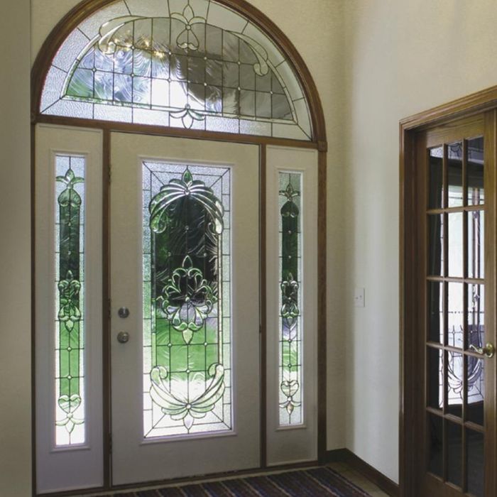 An interior view of a white front door with a large arched decorative glass insert and sidelights, showing high-clarity glass and intricate caming.