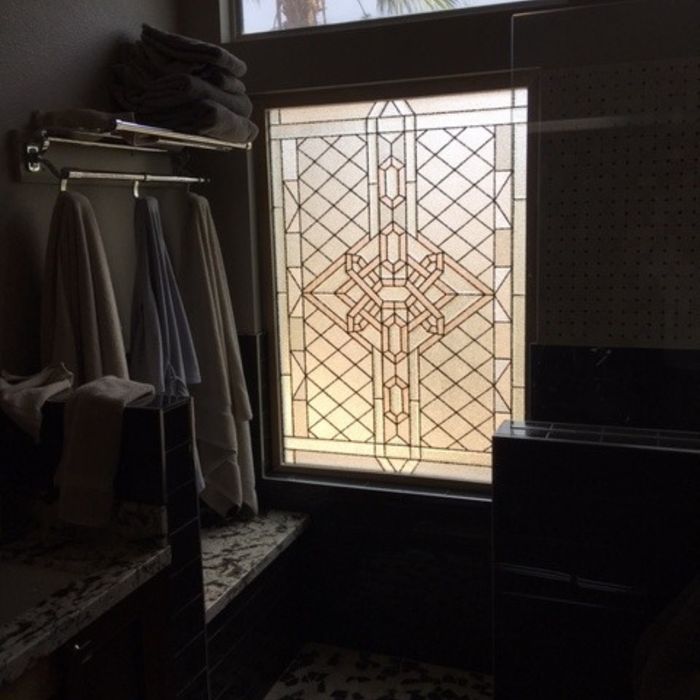 A large privacy window in a dark bathroom featuring a complex, amber-toned geometric glass design above a tiled vanity.