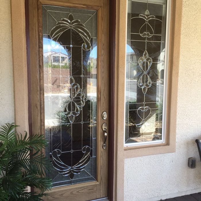 A close-up of a wooden front door with a full-length decorative glass insert featuring traditional leaded patterns and matching sidelights.