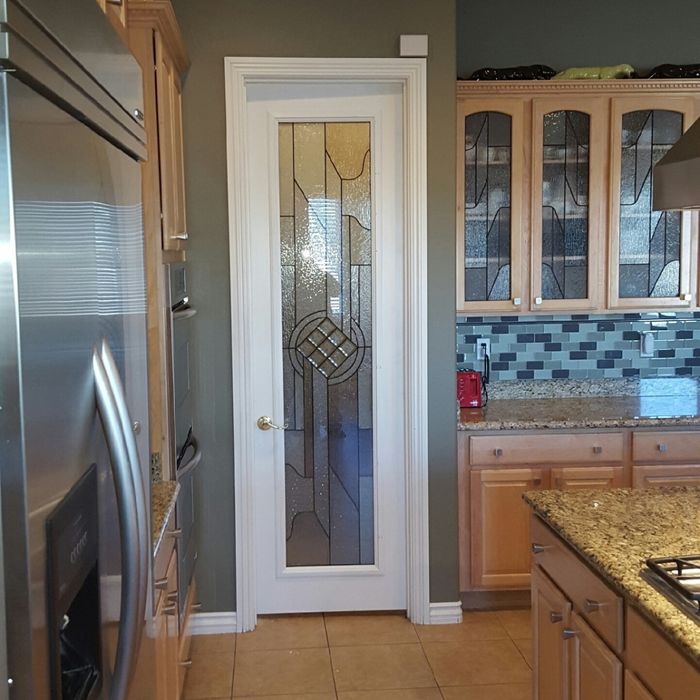 A white interior door with a large decorative glass insert featuring a geometric diamond design leading into a modern kitchen.