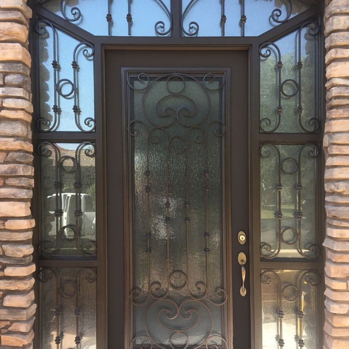 A brown front door featuring an ornate wrought iron design over textured glass, framed by rustic stone pillars and a decorative transom window.