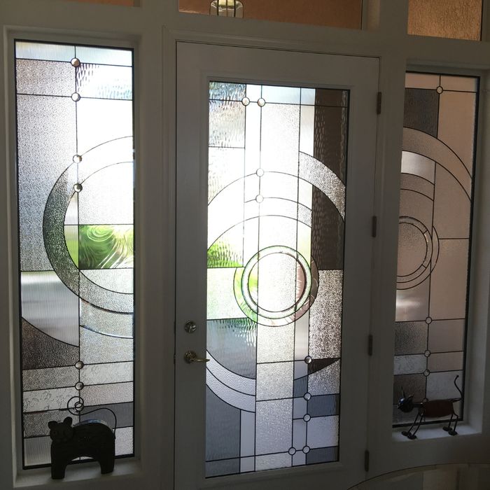 A modern white front door with matching sidelights featuring a minimalist geometric design of overlapping circles and lines.