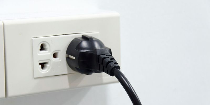 A close-up shot of a single black power cord plugged into a white electrical wall outlet.