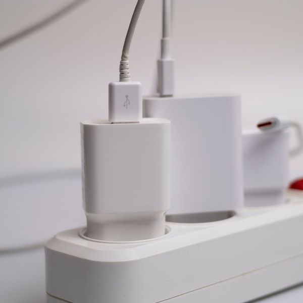 Multiple white power adapters and USB cables are plugged into a crowded white power strip.