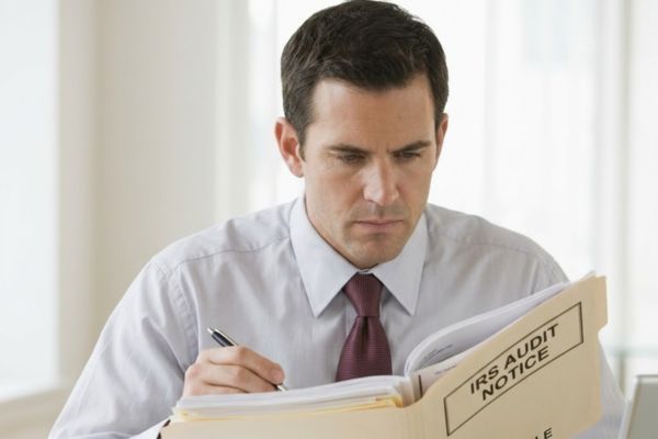 A focused professional man in an office examines a large file labeled 'IRS Audit Notice', depicting meticulous audit defense work.