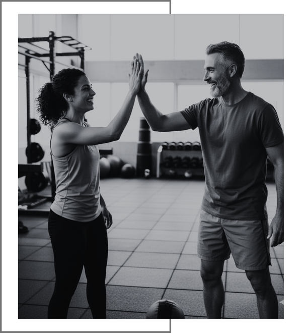 Two athletic friends smiling and high-fiving inside a gym, celebrating a completed workout together to promote the "Refer a Friend" savings program.