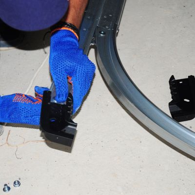 a person wearing gloves working on a garage door rail