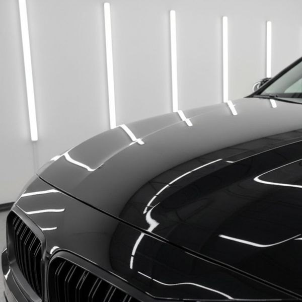 A black car with a highly reflective, glossy finish showcases perfect paint correction under bright vertical studio lights.