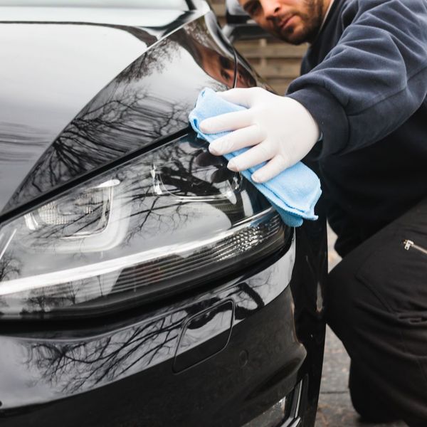 A dramatic close-up on a sleek, dark car's hood where a gloved hand applies clear paint protection film, while the adjacent surface shows perfect water beading, demonstrating a ceramic coating's hydrophobic effect. A dramatic close-up on a sleek, dark car's hood where a gloved hand applies clear paint protection film, while the adjacent surface shows perfect water beading, demonstrating a ceramic coating's hydrophobic effect.