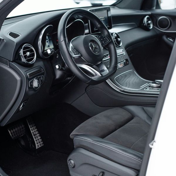 An interior shot of a clean, modern Mercedes-Benz SUV, focusing on the steering wheel, dashboard, and driver's seat. The image showcases the car's pristine condition and high-end features.