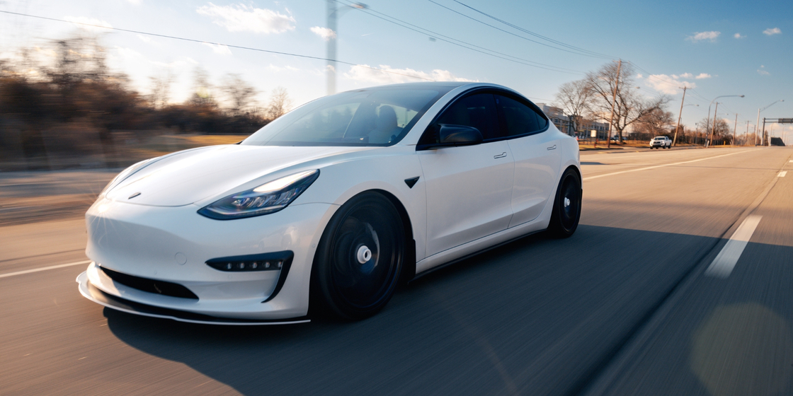 A sleek, white two-door car with black wheels is driving on a road under a bright sky, with trees and a blurred background suggesting motion. A sleek, white two-door car with black wheels is driving on a road under a bright sky, with trees and a blurred background suggesting motion.