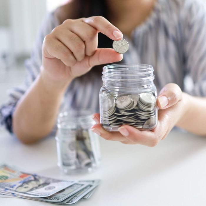 person putting coin in jar full of coins