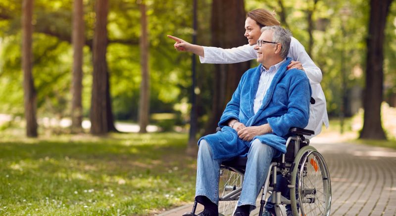 smiling caregiver pointing at something to show older man in wheelchair