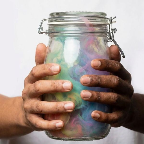 Hands tightly holding a sealed glass jar filled with swirling, colorful smoke.