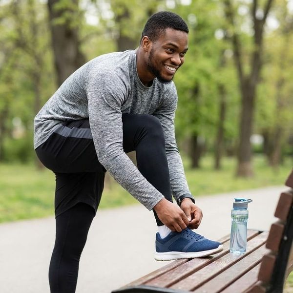 A Black man tying his running shoe on a park bench.