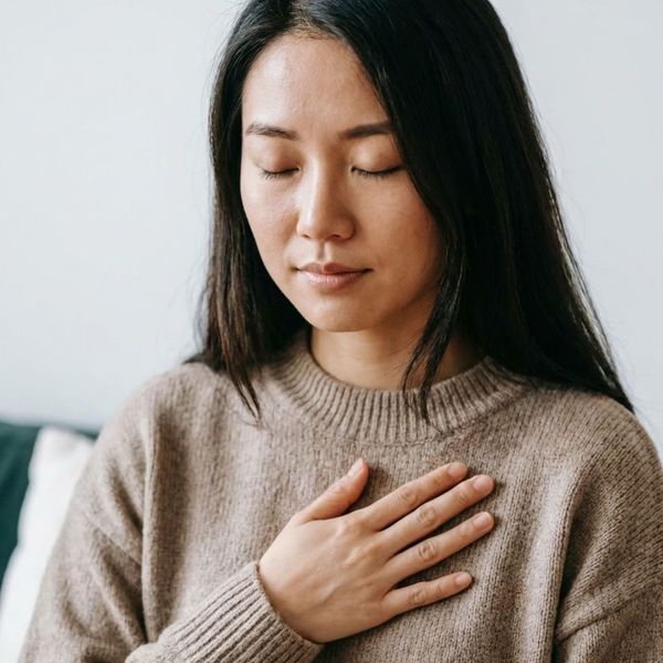 An East Asian woman with eyes closed, gently placing a hand over her heart.