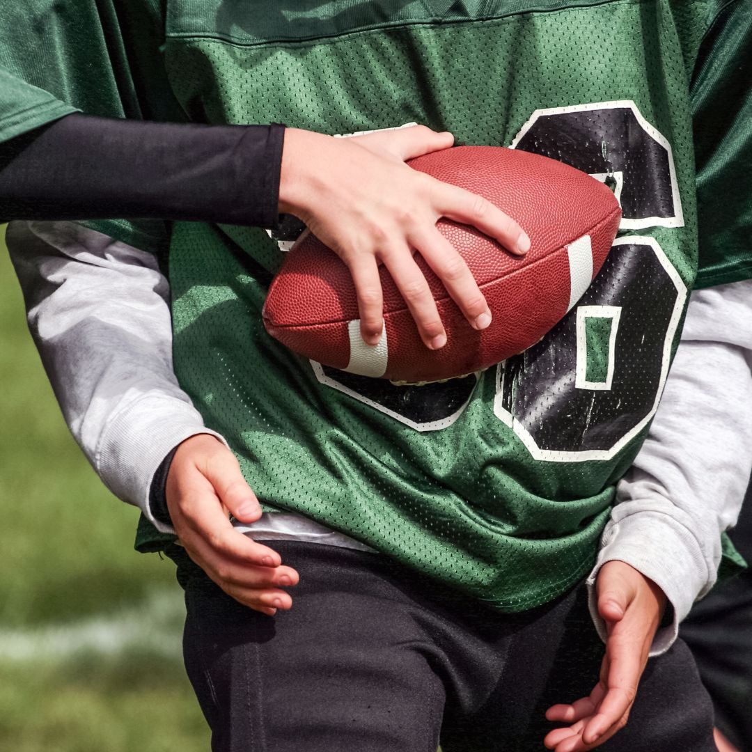 young kid handing another young kid a football