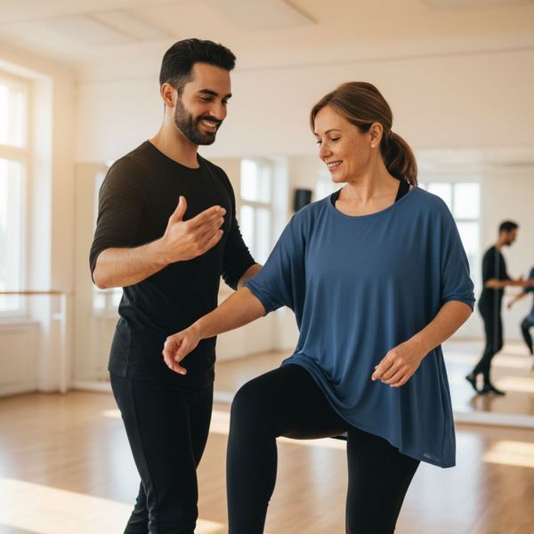 A smiling adult practices dance steps with an instructor in a bright studio.
