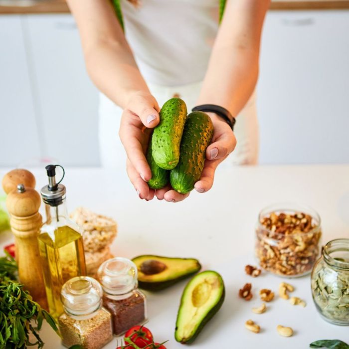 woman holding cucumbers near other healthy foods