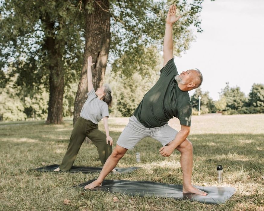 Two 50 year old people doing a yoga pose (triangle pose) outdoors in a grassy park, demonstrating active aging. Two 50 year old people doing a yoga pose (triangle pose) outdoors in a grassy park, demonstrating active aging.