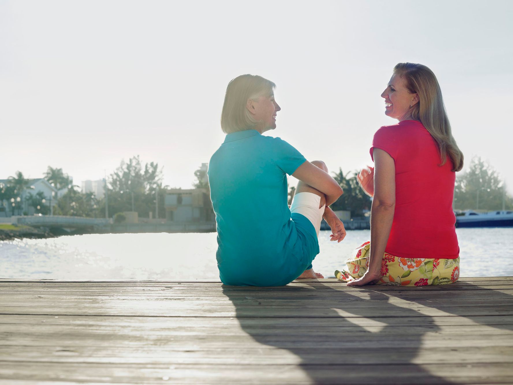 Two people sitting back-to-back on a wooden dock looking out over a calm body of water or lake. Two people sitting back-to-back on a wooden dock looking out over a calm body of water or lake.