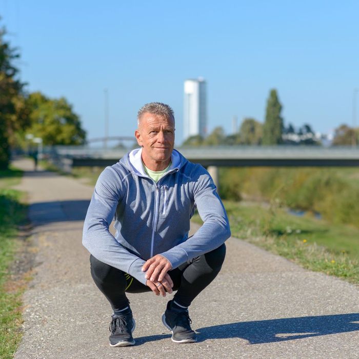 middle-aged man squatting for a break during a run