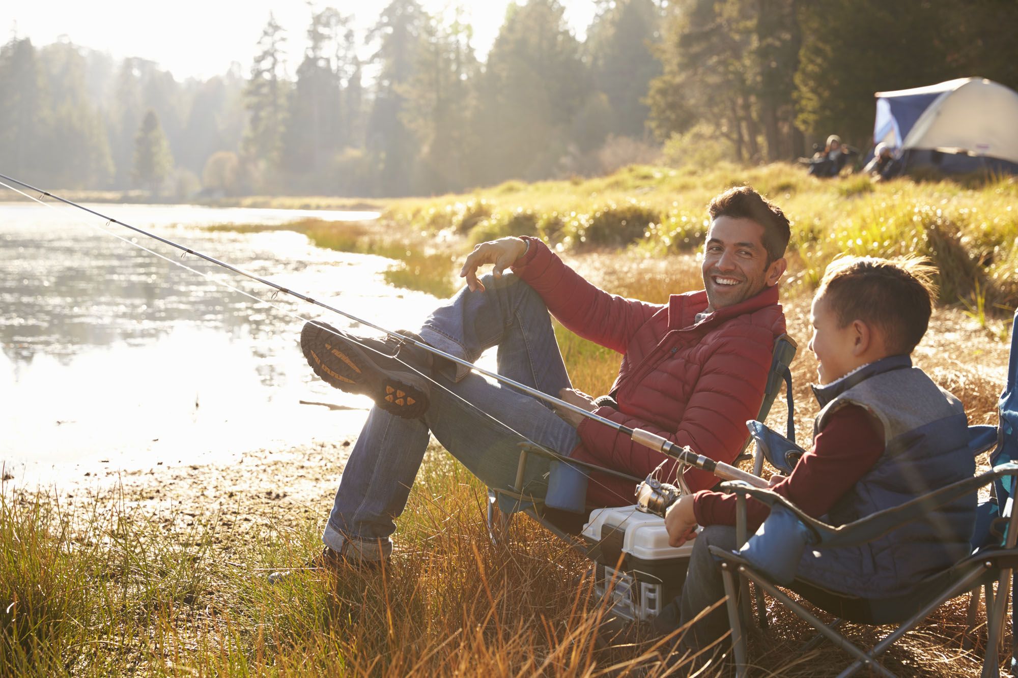 A family (mother, father, and child) sitting on the grass near a lake, fishing together on a sunny, hazy afternoon. A family (mother, father, and child) sitting on the grass near a lake, fishing together on a sunny, hazy afternoon.