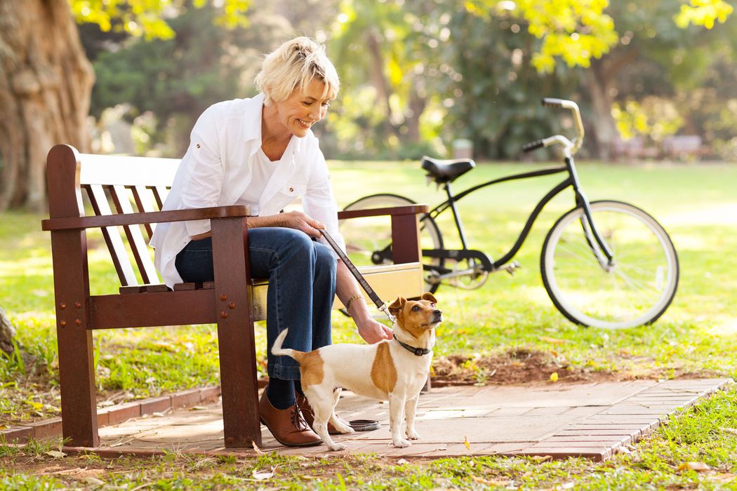 A woman sitting on a wooden park bench, happily petting her small dog with a bicycle parked nearby. A woman sitting on a wooden park bench, happily petting her small dog with a bicycle parked nearby.