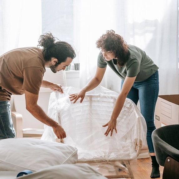 people wrapping chairs in moving plastic