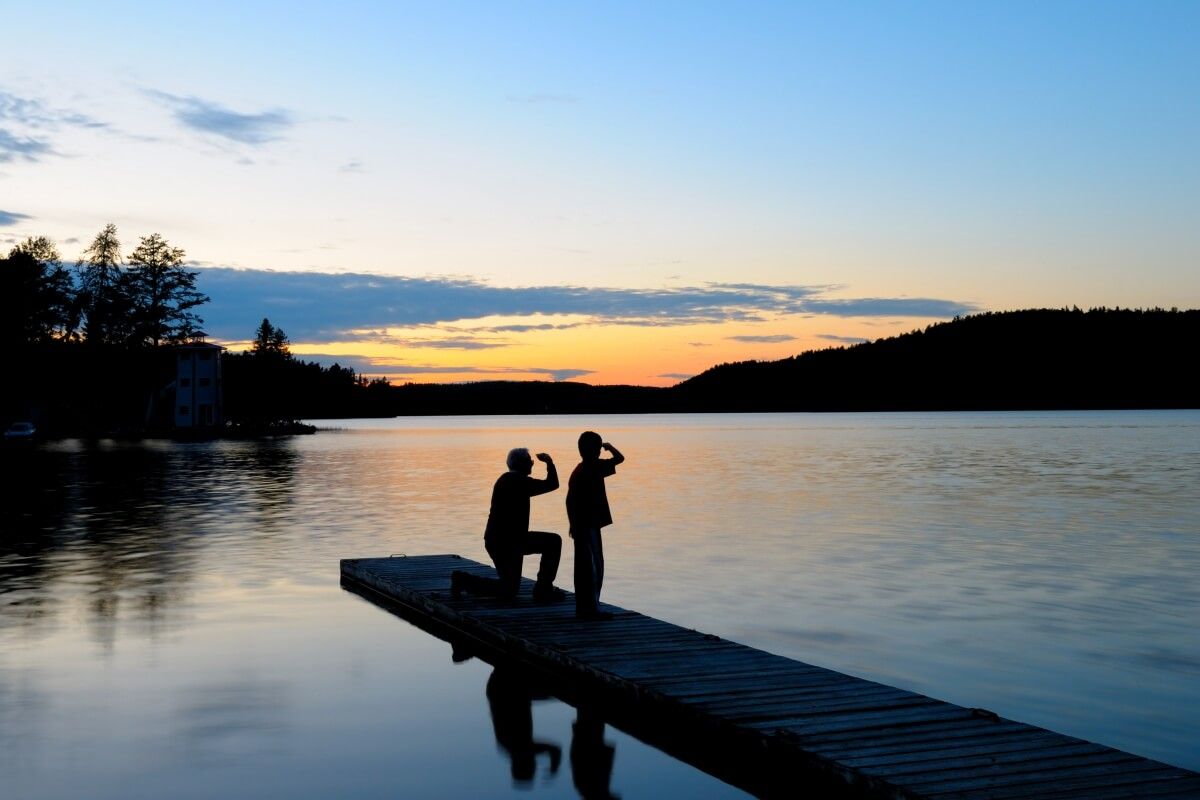 Two people sitting at a dock at sunset.