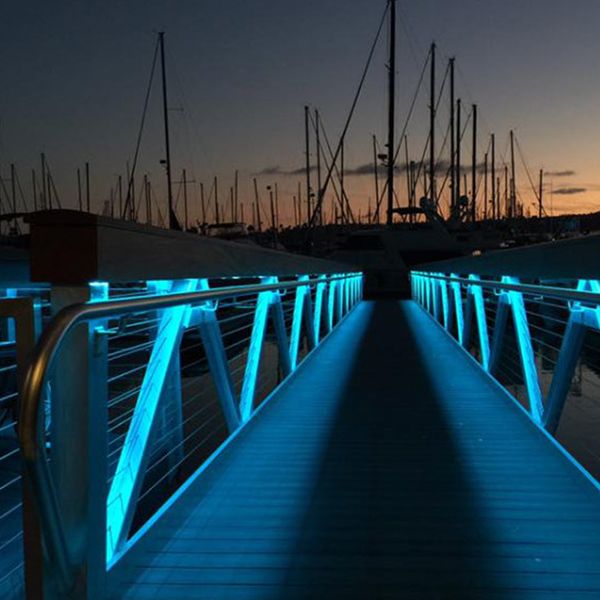 A beautiful dock lit up with blue lights on the hand rails with views of sailboats in the background.