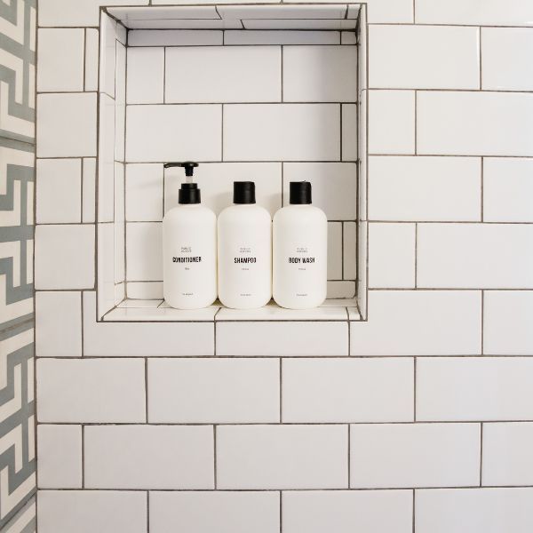 a white tile shower niche with shampoos