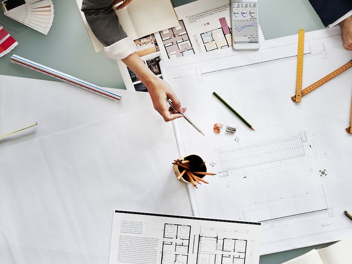 An overhead image of a bunch of people sitting at a table with drafting plans sprawled out.