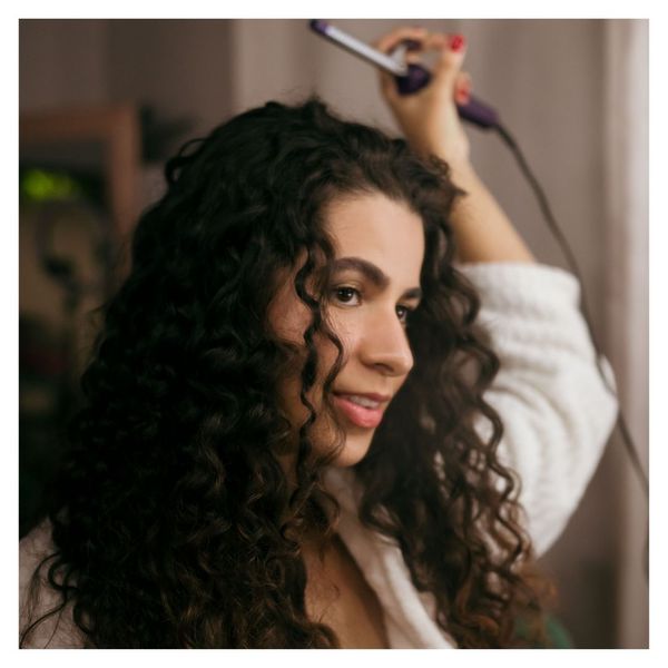 woman with curly hair holding curling iron