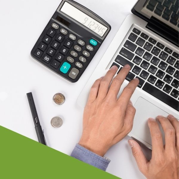 Someone using a Mac with a calculator and coins sitting next to their computer