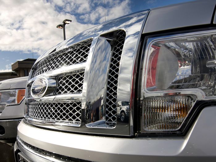 close up of truck grill, with multiple trucks parked at car dealership