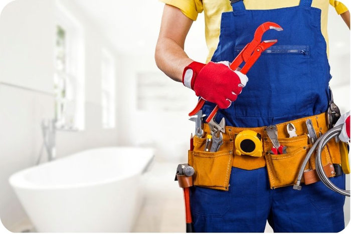 Plumber standing in a bathroom, holding tools. 