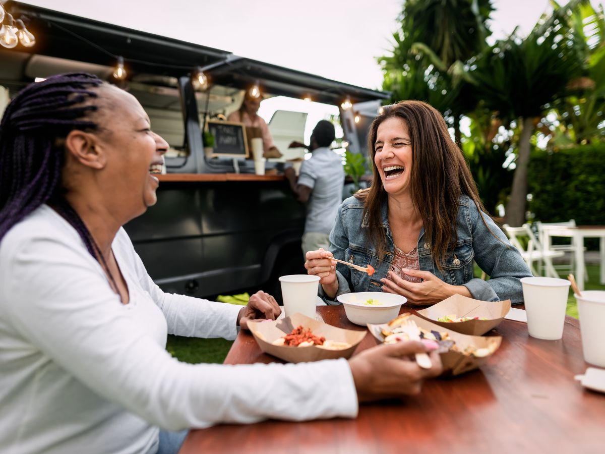 two happy woman eating from food truck two happy woman eating from food truck