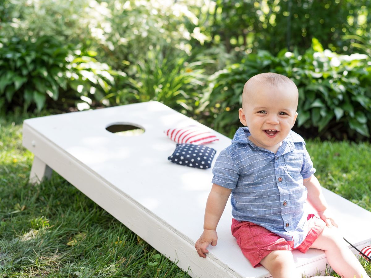 happy toddler sitting on cornhole board happy toddler sitting on cornhole board