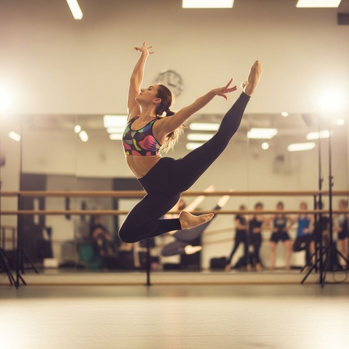 A female dancer mid-leap showing dynamic energy and flexibility in a brightly lit jazz class.
