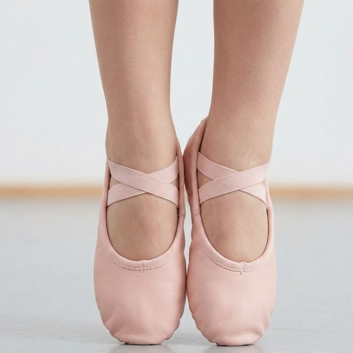 Pink leather ballet slippers are tied neatly on a young child's feet.