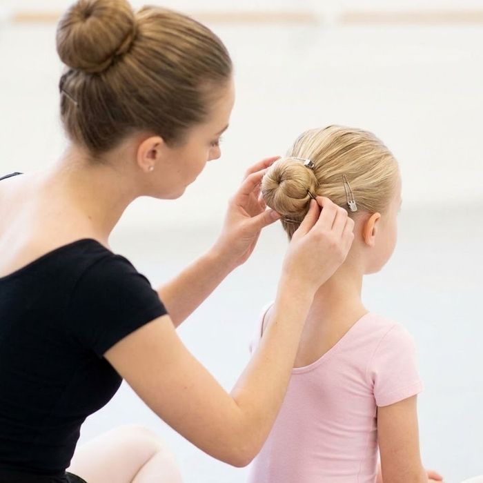 An instructor tidying a young girl's hair into a secure ballet bun