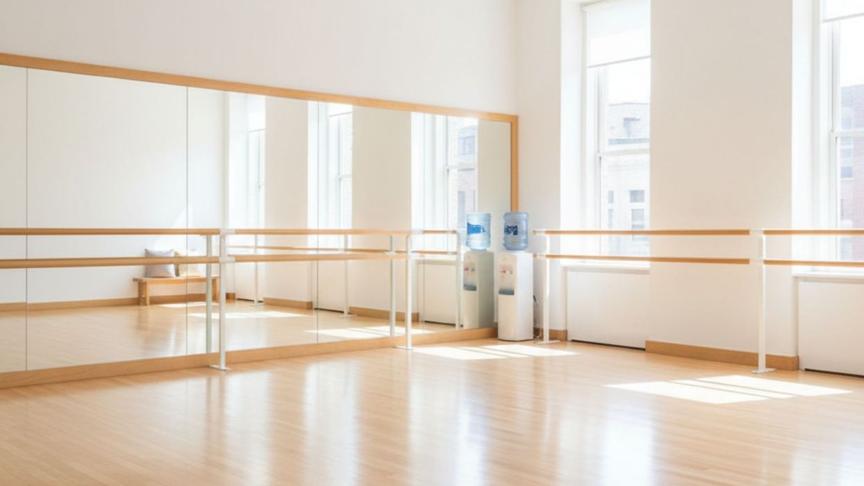 A bright, empty, professional dance studio with wood floors and wall-length mirrors.
